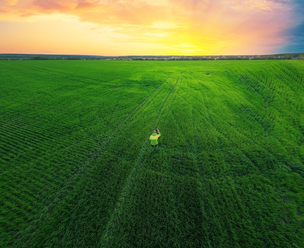 Le photographe dans un champ vert avec un appareil photo sur un trépied photographie le coucher du soleil