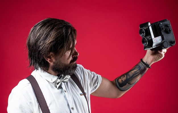 Un photographe élégant et confiant tient un journaliste de caméra classique avec un appareil photo vintage, un journaliste de fête formelle, un hipster barbu à l'ancienne, un homme rétro en bretelles et un selfie avec un nœud papillon