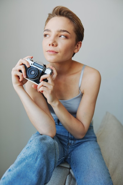 Photographe féminine tournant en studio sur une vieille caméra de film à la maison sur le canapé portrait fond blanc espace de copie libre photographe indépendant photo de haute qualité