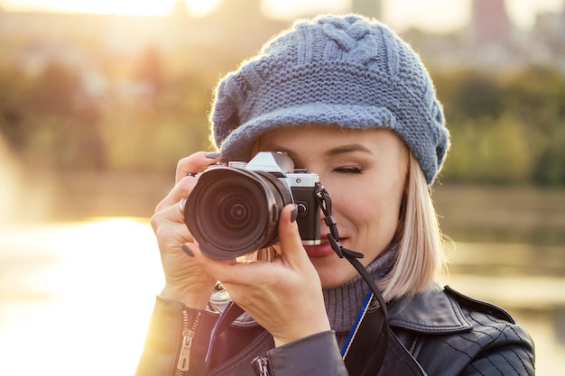 Photographe femme blonde élégante prend des photos de la forêt d'automne au coucher du soleil