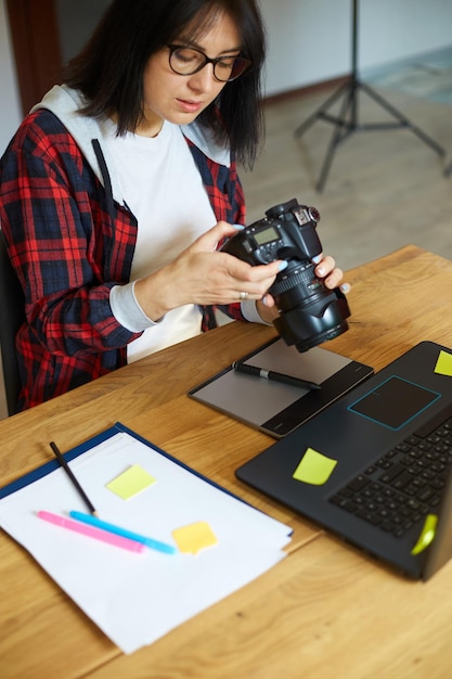 Photographe femme travaillant dans un bureau créatif tenant un appareil photo au bureau et retoucher la photo