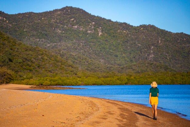 photographe fille au chapeau se promène le long de la plage paradisiaque sur l'île magnétique au coucher du soleil, australie