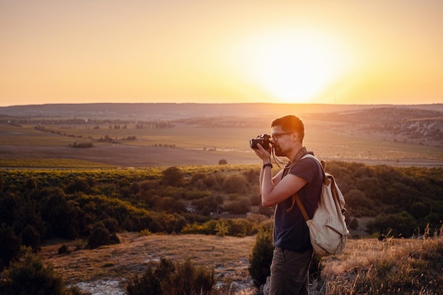 Photographe homme avec sac à dos et appareil photo prenant des photos de montagnes au coucher du soleil