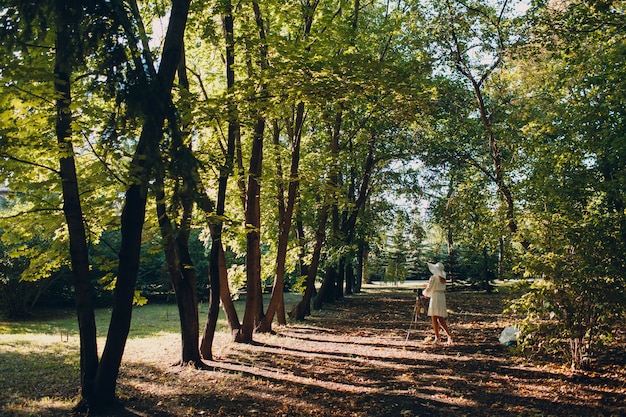 Photo photographe de jeune femme en robe blanche et chapeau avec appareil photo en automne parc.