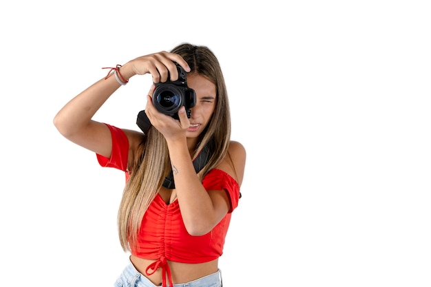 Photographe de jeune femme avec son appareil photo à la main en prenant une photo avec un fond blanc.