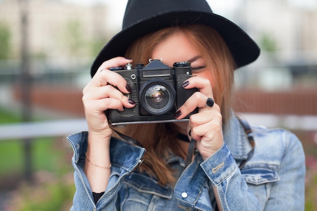 Photographe de jeune fille marchant le long de la rue dans une veste de jeans avec un vieil appareil photo