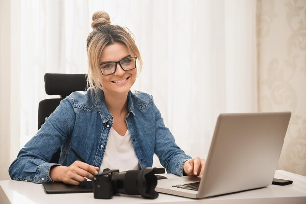 Photographe jeune et heureuse avec un appareil photo sans miroir sur le lieu de travail