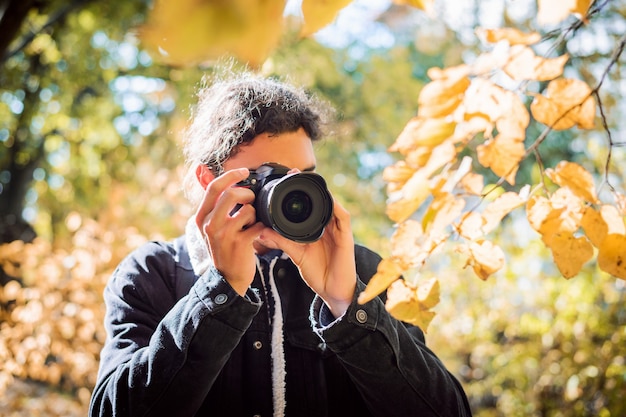 Photographe de jeune homme aux cheveux bouclés foncés dans le parc d'automne