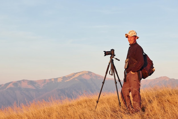 Photographe masculin debout et travaillant dans un paysage majestueux d'arbres d'automne et de montagnes à l'horizon