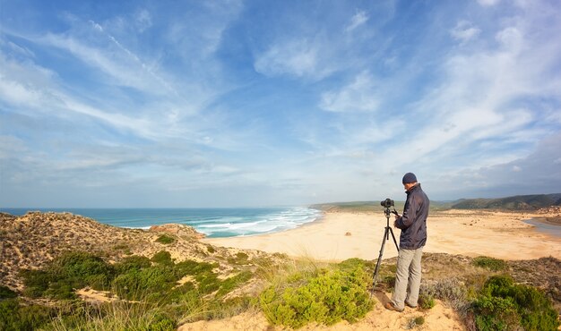 Photographe masculin voyageant et photographie dans les dunes. Avec trépied et appareil photo.