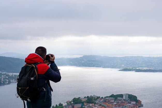 Photographe méconnaissable avec son sac à dos sur le dos et photographiant la ville de Bergen et le fjord en Norvège