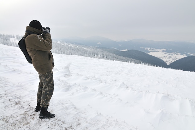 Un photographe prenant une photo d'une incroyable montagne hivernale depuis le sommet d'une montagne.