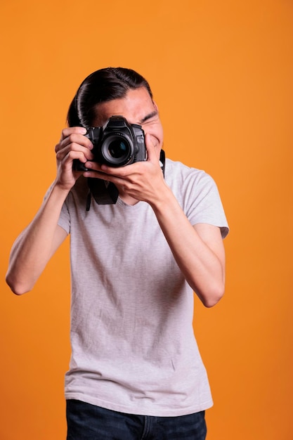 Photographe prenant des photos sur un appareil photo numérique professionnel, regardant dans le viseur. Jeune homme asiatique utilisant un équipement de photographie, vue de face, plan moyen, passe-temps créatif, séance photo