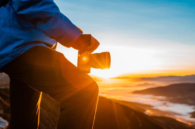 Un photographe relaxant sur le sommet de la montagne au lever ou au coucher du soleil voyage d'aventure