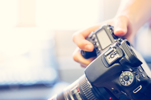 Le photographe tient un appareil photo reflex avec téléobjectif dans sa main Table et ordinateur portable dans l'arrière-plan flou