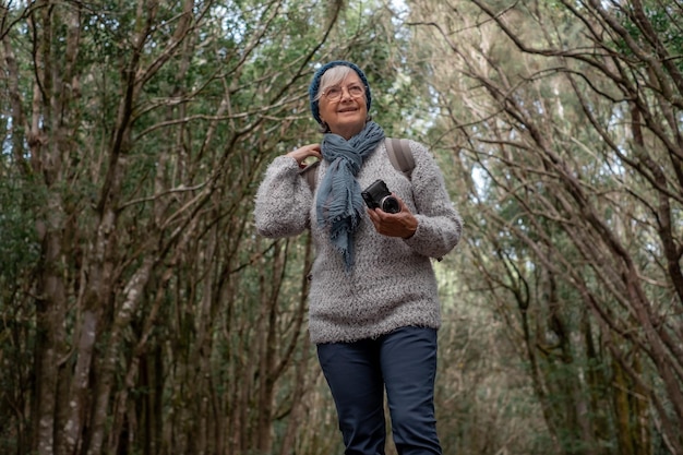 Photographe touristique souriante femme senior en excursion en plein air dans la forêt tenant un appareil photo