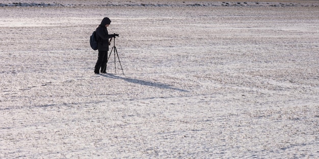 Un photographe avec un trépied dans un champ enneigé prend des photos d'empreintes de paysage d'hiver dans la neige