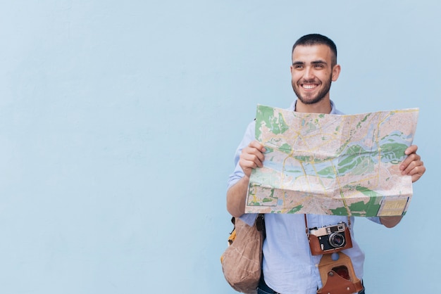 Photographe voyageur souriant tenant la carte et regardant loin debout contre fond bleu