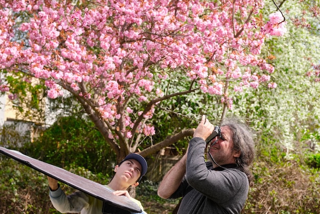 Photographes père et fils tirant des fleurs de Sakura au printemps Le fils assiste avec un réflecteur le père qui photographie des fleurs Une activité de loisirs en famille