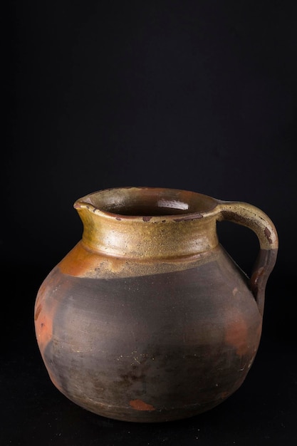 Photo photographie d'une cruche de céramique antique fonctionnelle et de poterie domestique représentée sur un fond noir