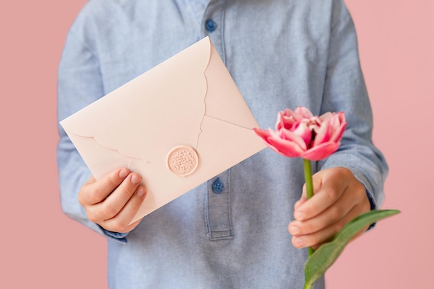 Photo photographie en gros plan d'un enfant tenant dans les mains un cadeau de certificat rose avec sceau de cire et tulipe