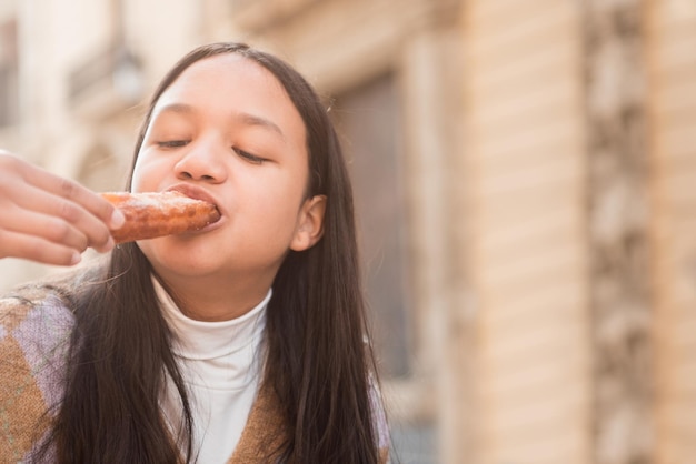 Photographie en gros plan d'une jeune adolescente brune appréciant de manger des churros à l'extérieur