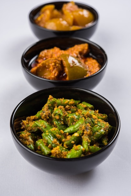 Photographie de groupe de cornichons indiens comme le cornichon à la mangue, le cornichon au citron et le cornichon au piment vert, conservés dans un bol en céramique noire, mise au point sélective