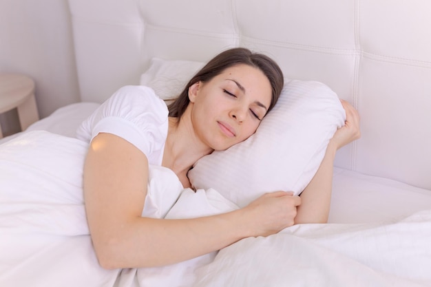 Photographie jeune femme endormie se trouve dans son lit avec ses yeux fermés sur un blanc