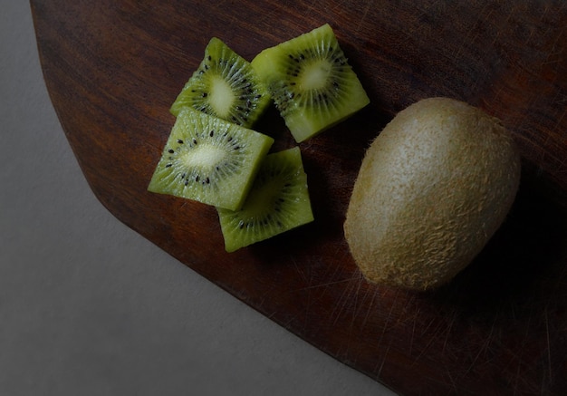 Photographie d'un kiwi entier coupé en cubes sur un fond de bois sombre