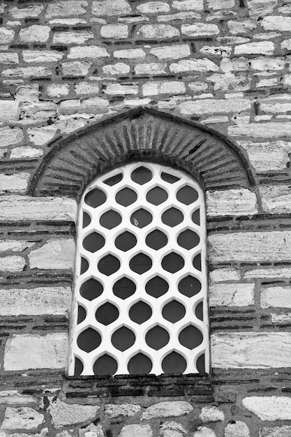 Photographie noir et blanc Une fenêtre avec un treillis blanc ajouré dans le mur d'un vieux bâtiment en pierre