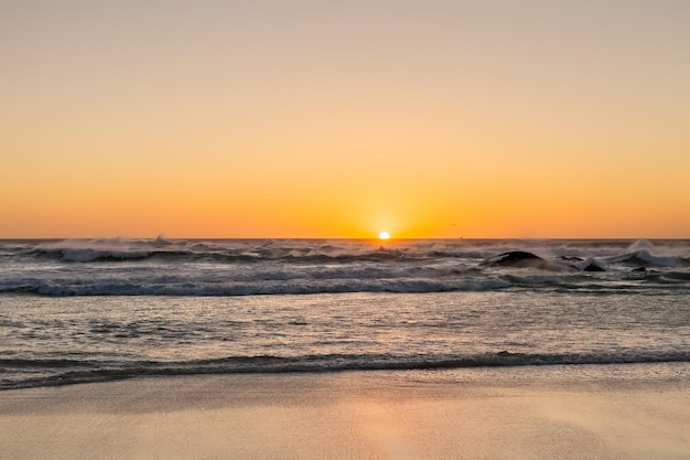 Photographié sur une plage face à la côte ouest du Cap en Afrique du Sud. Vagues agitées au coucher du soleil sur une plage de sable avec des reflets sur l'eau