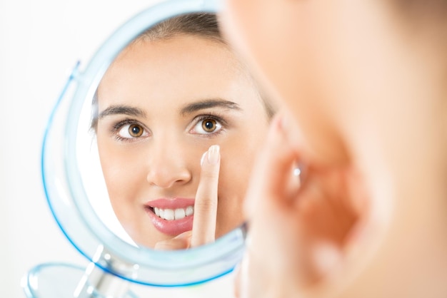 Photographie de reflet dans le miroir, belle fille qui a appliqué la crème sur son visage.