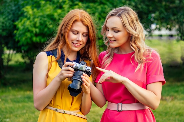 Photosession belle jeune fille irlandaise rousse au gingembre dans une robe jaune et une femme blonde européenne en robe rose se sont photographiées dans le parc d'été séance photo de deux copines modèles