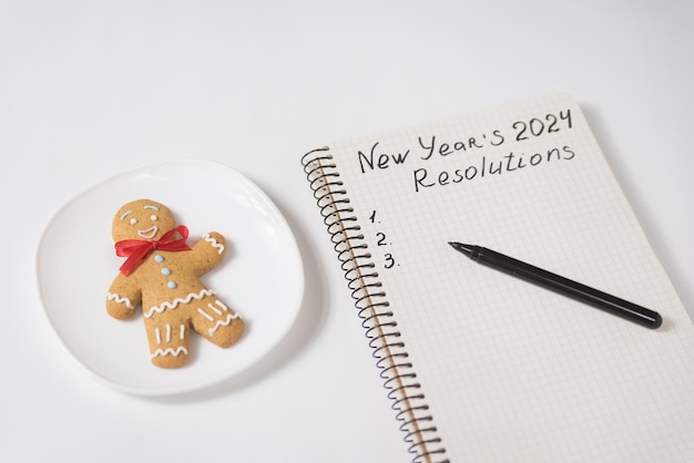 Phrase Résolutions de la nouvelle année 2024 dans le cahier et le stylo Gingerbread homme sur la table