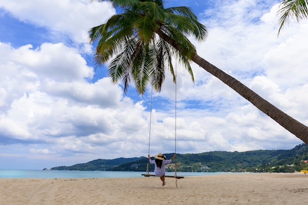 Phuket Thaïlande Paradis de plage tropicale avec balançoire de plage avec une fille en chemise blanche Les femmes se détendent sur une balançoire sous un cocotier sur une belle plage tropicale Sable blanc
