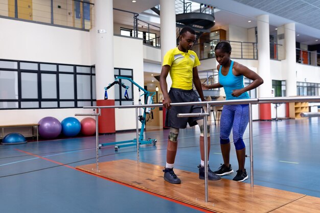 Photo physiothérapeute aidant un homme handicapé à marcher avec des barres parallèles dans un centre sportif