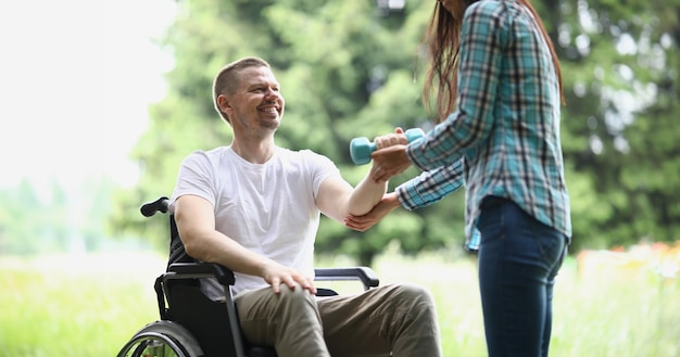 Photo une physiothérapeute aide un jeune homme en fauteuil roulant à soulever le poids des bras dans le parc rééducation des personnes handicapées et activité physique