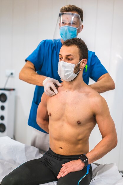 Un physiothérapeute donnant un massage à une clavicule à un patient. Physiothérapie avec mesures de protection contre la pandémie de coronavirus, COVID-19. Ostéopathie, chiromassage thérapeutique