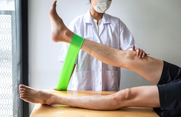 Physiothérapeute féminine travaillant sur le traitement de la jambe blessée d'un patient masculin, faisant des exercices de la douleur de thérapie de réadaptation en clinique.