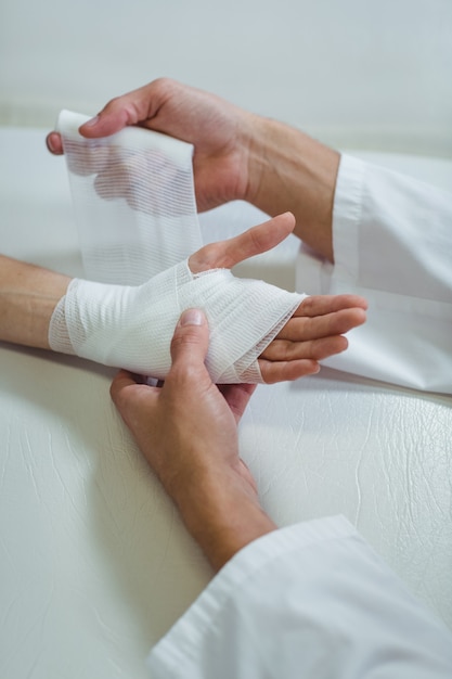 Physiothérapeute mettant un bandage sur la main blessée du patient