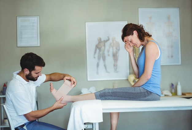 Physiothérapeute mettant un bandage sur les pieds blessés du patient