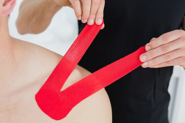 Physiothérapeute mettant sur le ruban rouge de Kinesio sur l&#39;épaule des patients