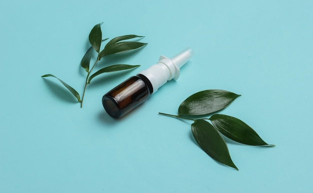 Phytothérapie pilules blanches spray nasal avec des feuilles vertes sur fond bleu