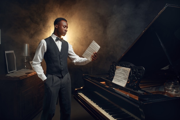 Pianiste ébène avec cahier de musique dans ses mains sur la scène avec des projecteurs. interprète pose à l'instrument de musique avant concert