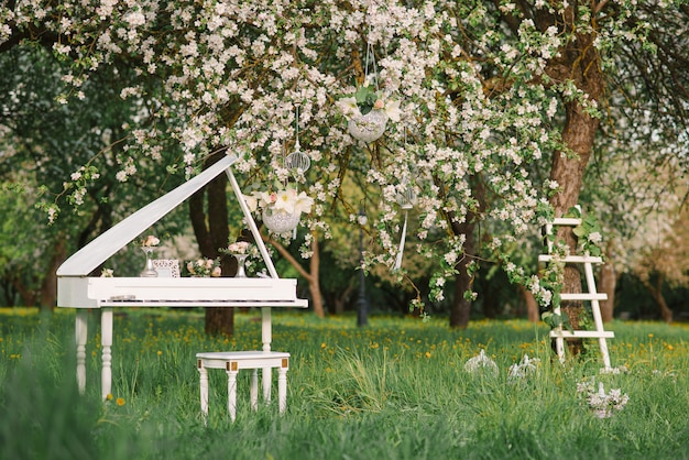 Piano à queue blanc et escalier blanc au décor romantique au printemps dans un jardin de pommiers en fleurs