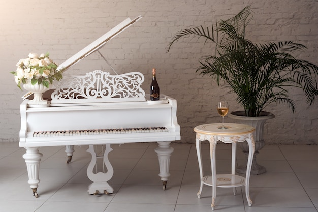Piano à queue dans un intérieur classique de luxe blanc avec du vin, des palmiers et des fleurs.