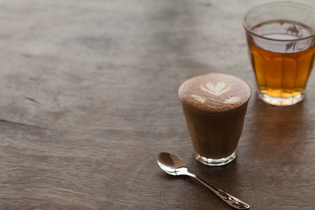 Piccolo Latte art dans un petit verre avec du thé chaud sur un bureau en bois