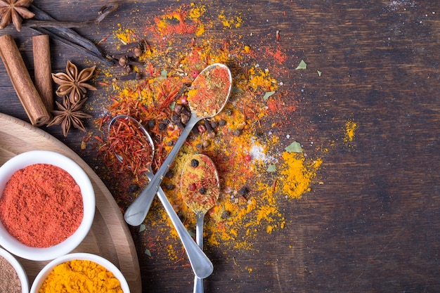 Épices colorées dans des cuillères sur une table en bois sombre, vue du dessus