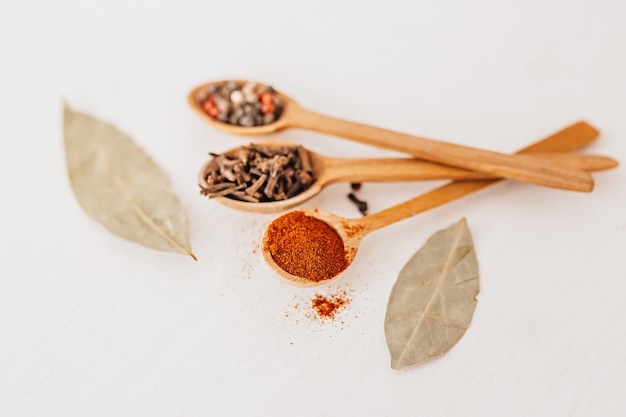 Épices dans une cuillère en bois. Herbes, curry, safran, curcuma, cannelle, laurier, poivrons pour la cuisson sur fond blanc