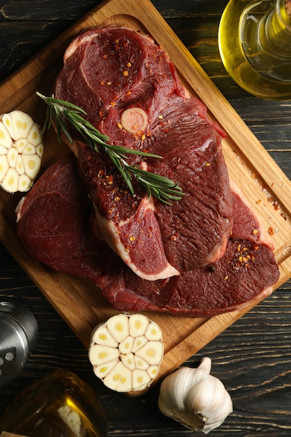 Épices, huile et planche avec de la viande de steak crue sur bois